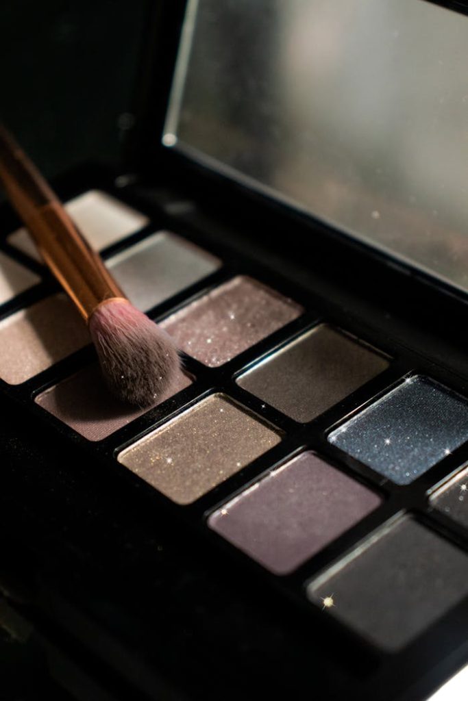 Detailed image of an eyeshadow palette with a makeup brush resting on it, showing various shades.